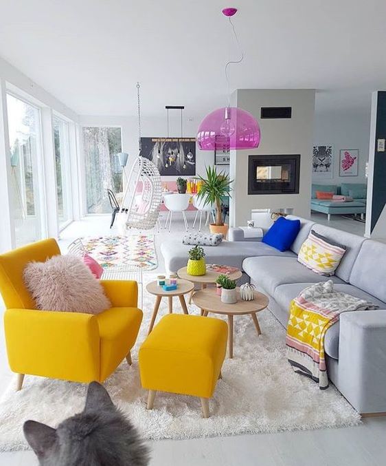 A neutral living room with a bright yellow chair, boho textiles, a pink pendant lamp and potted plants.