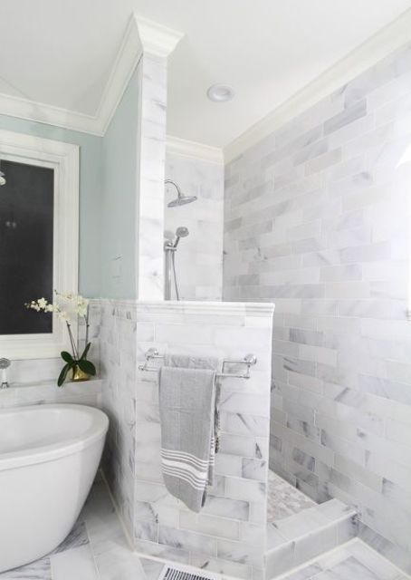 A neutral marble bathroom with a shower space with a pony wall, a bathtib and blue walls is very refined.
