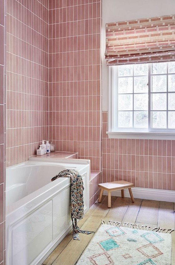 A pastel pink bathroom with skinny tiles, a bathtub and several built-in shelves, a blush curtain and a boho rug.