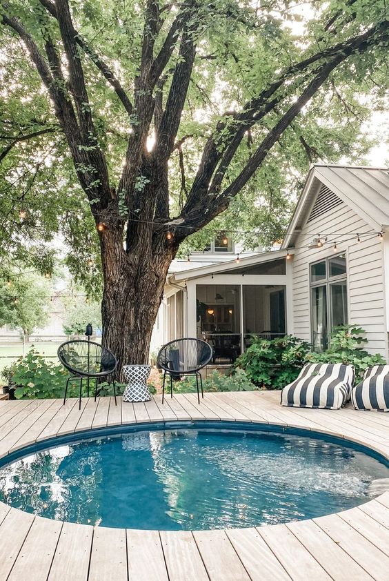 A peaceful outdoor space with a tank pool and a wooden deck around it, striped loungers and black chairs plus a side table.