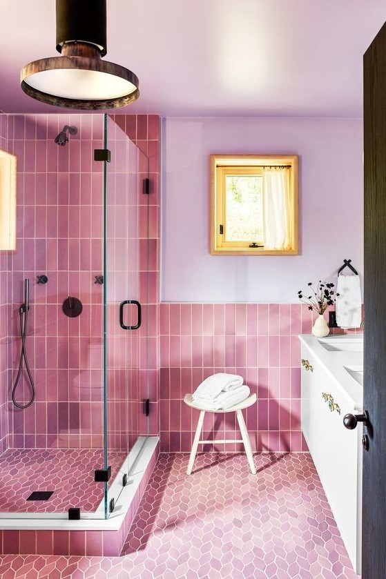 A pink and lilac bathroom with lilac walls, pink skinny and leafy tiles, a white vanity and black fixtures.