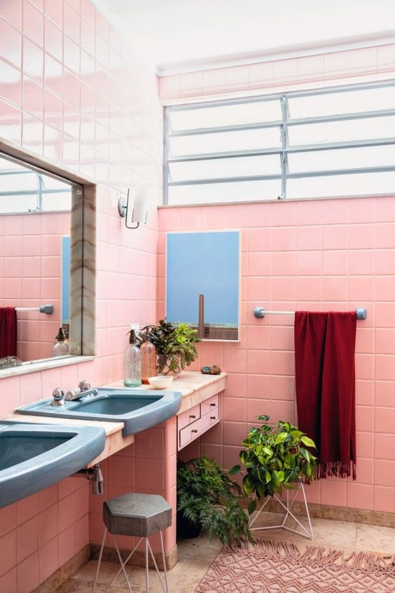 A pink bathroom with a tiled vanity and blue sinks, mirrors, potted plants and a pink boho rug is amazing.