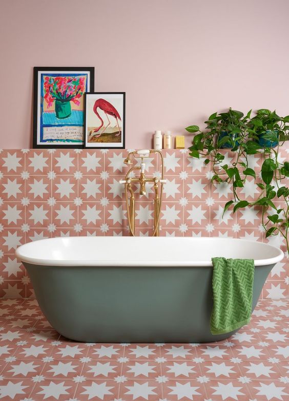 A pink bathroom with light pink walls, beautiful star-printed tiles, a green tub, some decor and potted greenery.