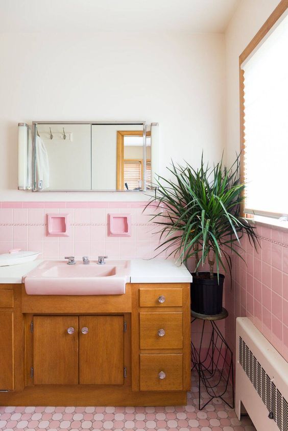 A pretty mid-century modern bathroom with light pink and printed pink tiles, a stained vanity, a mirror cabinet and a potted plant.