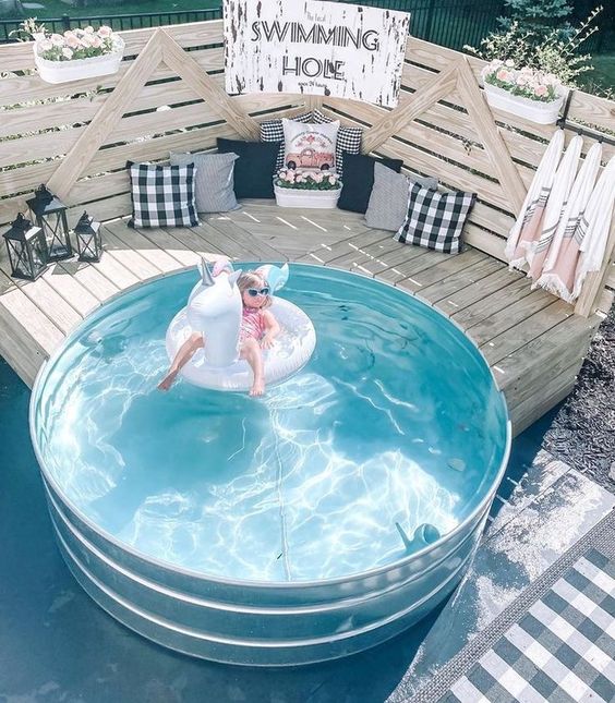 A pretty outdoor space with a stock tank pool, a wooden bench around it and some pillows and decor.