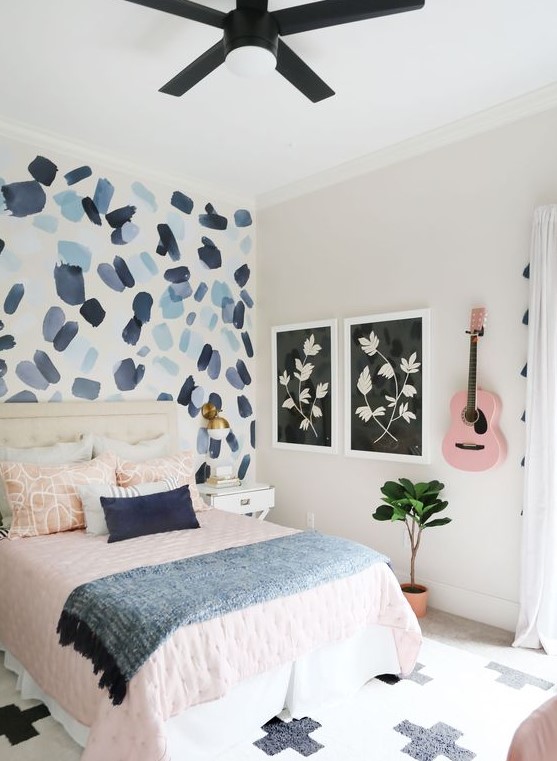 Create a pretty teen bedroom featuring a brushstroke accent wall and pink and blue textiles. The pink guitar on the wall adds a personal and artistic element. This room design offers a vibrant and unique space.