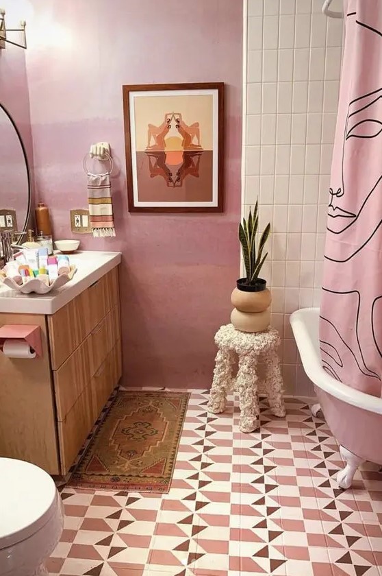 A pink free-standing bathtub and curtain add a quirky touch to this bathroom with geo tiles on the floor. A light-stained vanity provides warmth and balance. Opt for colorful fixtures and light wood to create an eye-catching bathroom.