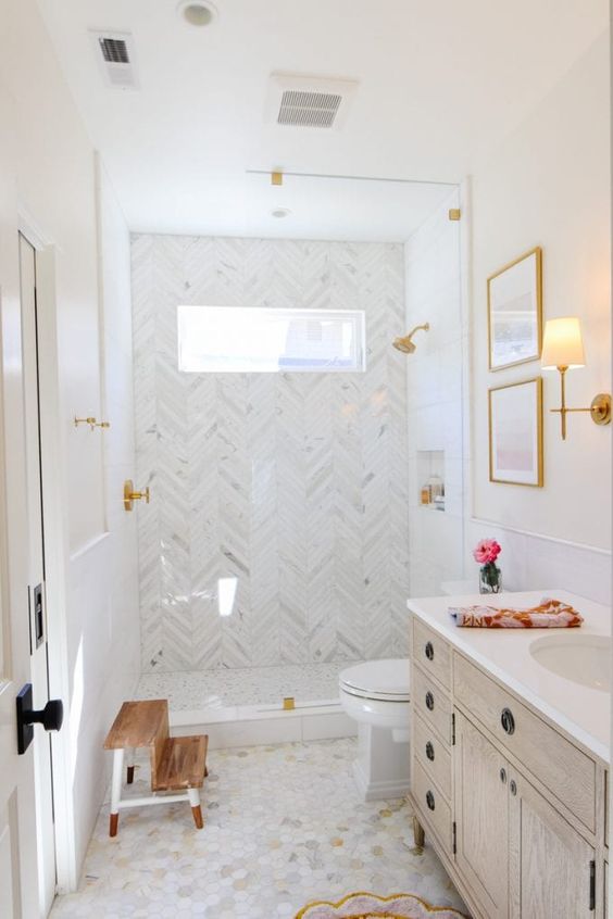 A refined neutral bathroom with herringbone and marble tiles, a shower space, a stained vanity and gold fixtures.