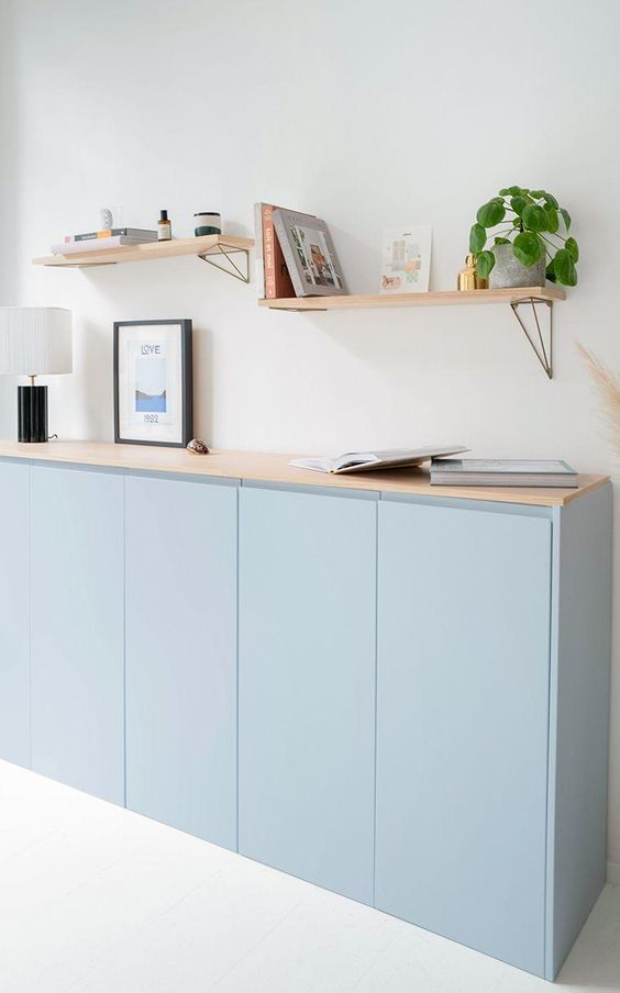 A serene light blue sideboard made of an IKEA Metod cabinet, with a wooden countertop, with books and decor and some shelves over.