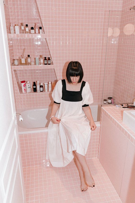 A small and lovely pink bathroom clad with small scale tiles, a tub, a tile vanity, niche shelves and white appliances.