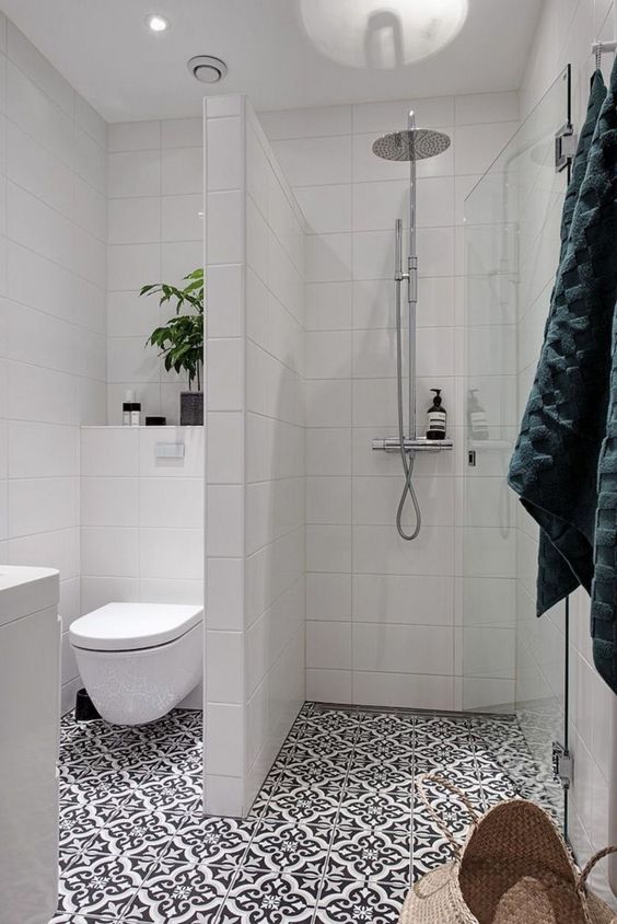 A small bathroom with a shower separate with white long tiles, a printed tile floor, a potted plant and a white vanity.