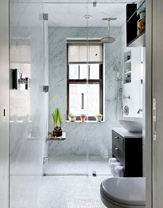 A small bathroom with blue stone tiles in the shower, a dark stained vanity, potted greenery and built-in shelves.