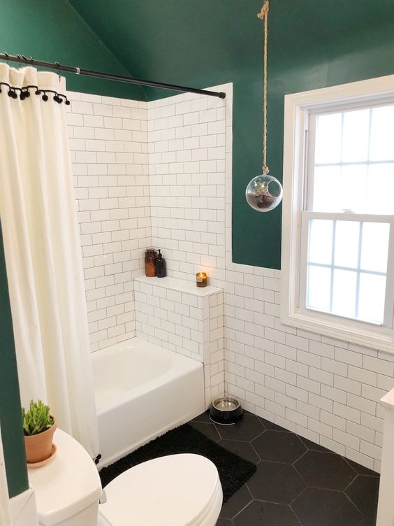 A small catchy bathroom with dark green walls and a ceiling, white subway tiles, black hex ones, a shower space and a window.
