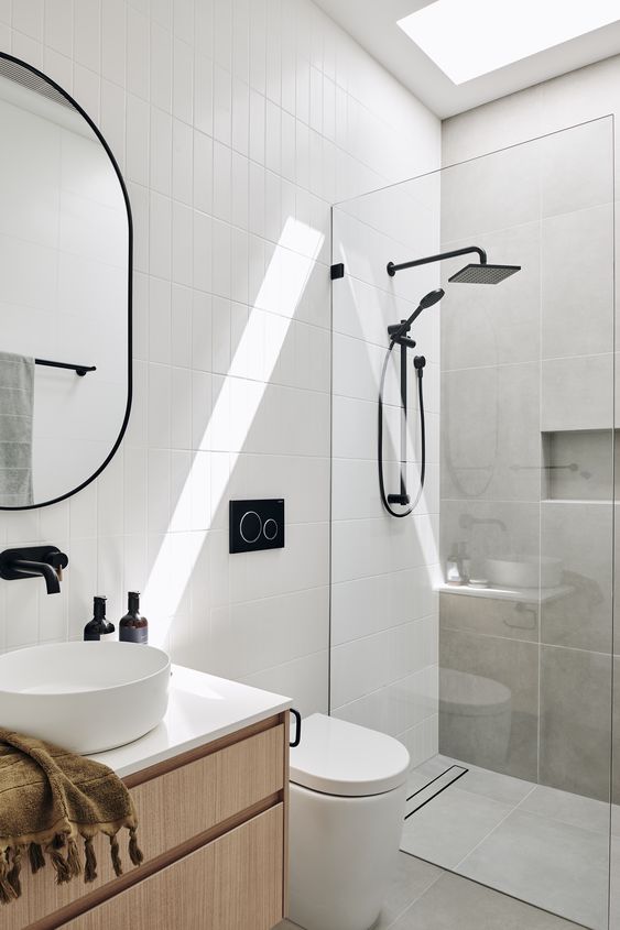A small contemporary bathroom clad with grey concrete and white skinny tiles, with a stained vanity and black fixtures.