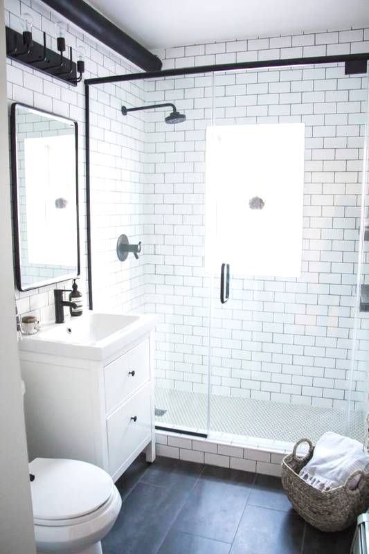 A small contemporary bathroom with white subway tiles, black tiles on the floor, a tiny vanity and black fixtures.
