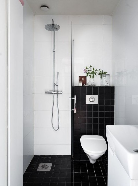A small contrasting bathroom with black and white tiles, a shower space, a sink and greenery to refresh the look.