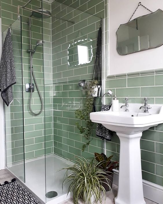 A small green bathroom clad with green subway tiles, with a shower, a free-standing sink and a mirror of a catchy shape.