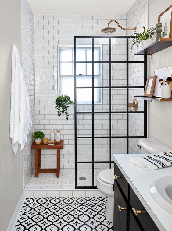 A small monochromatic bathroom clad with printed and white subway tiles, a black vanity, a black framed glass divider and brass touches.