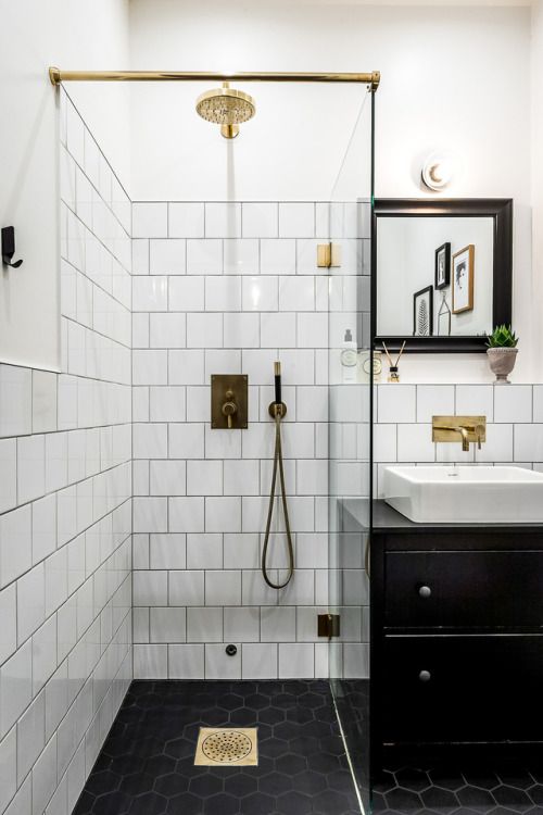 A small monochromatic bathroom with white and black hex tiles, a black vanity and a black frame mirror plus touches of gold.