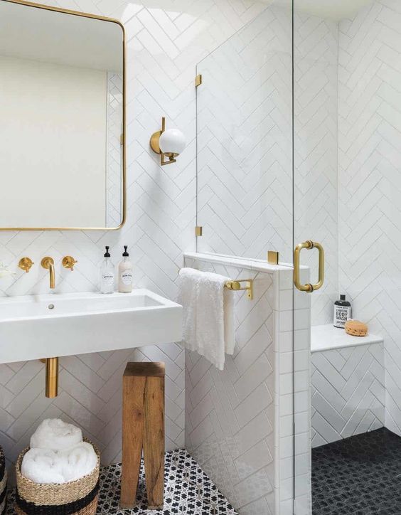 A small monochromatic bathroom with white herringbone tiles, printed black ones on the floor and touches of gold.