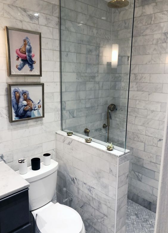 A small neutral bathroom with marble tiles, a shower space with a half wall, a small and fun gallery wall.