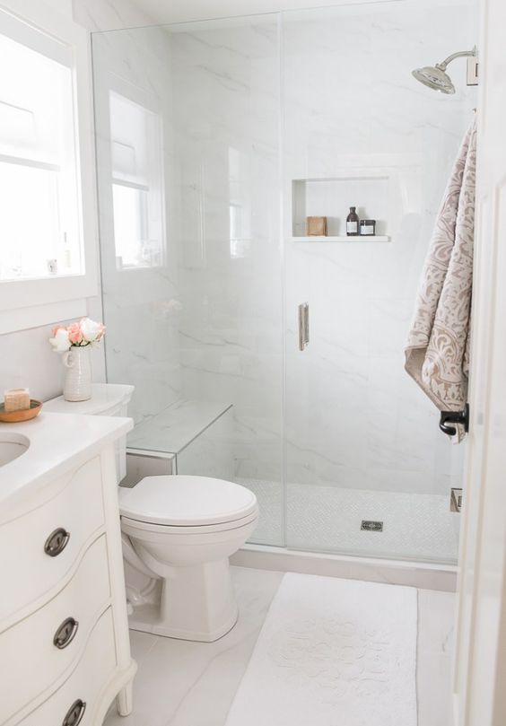 A small neutral bathroom with white marble tiles, a shower space, a white vanity, some neutral textiles is cool.