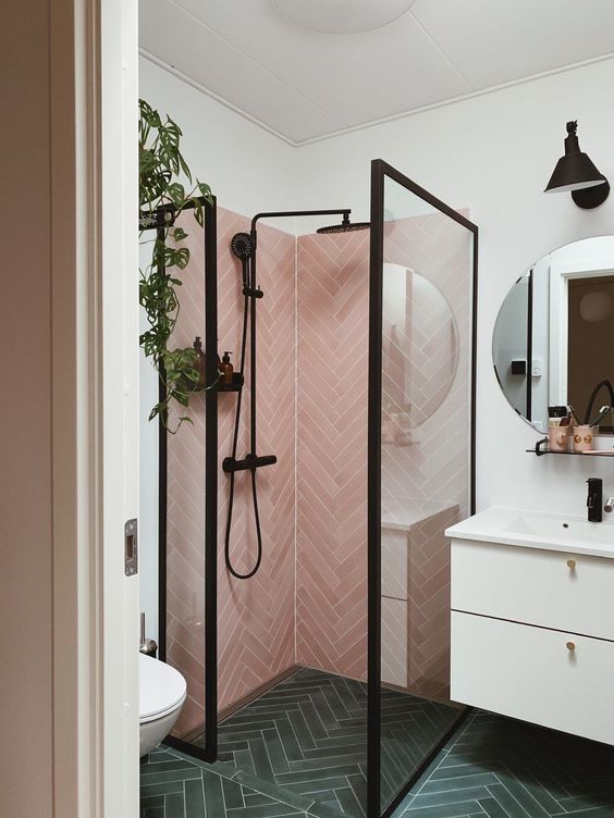 A small yet catchy bathroom with pink herringbone tiles and grene ones, a white vanity and black fixtures here and there.