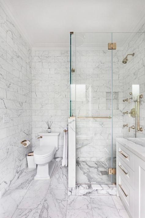 A sophisticated wihte marble tile bathroom with a shower space with a half wall, a white vanity and gold touches for more elegance.