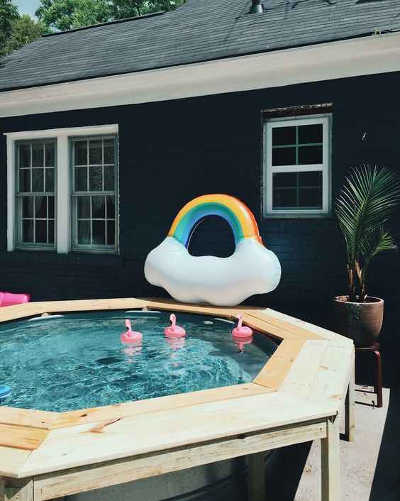 A stock tank pool surrounded by a wooden bench creates a cozy outdoor spot. Floats add a fun touch, while a potted plant brings in greenery. The combination makes this setup amazing and inviting.