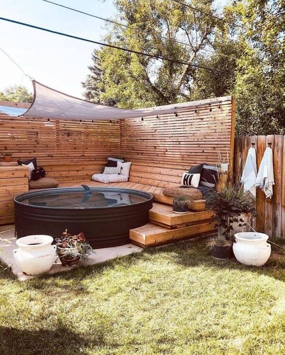 A stylish pool nook with a black stock tank pool, planked screens, wooden ladders and a bench, potted plants and printed pillows.