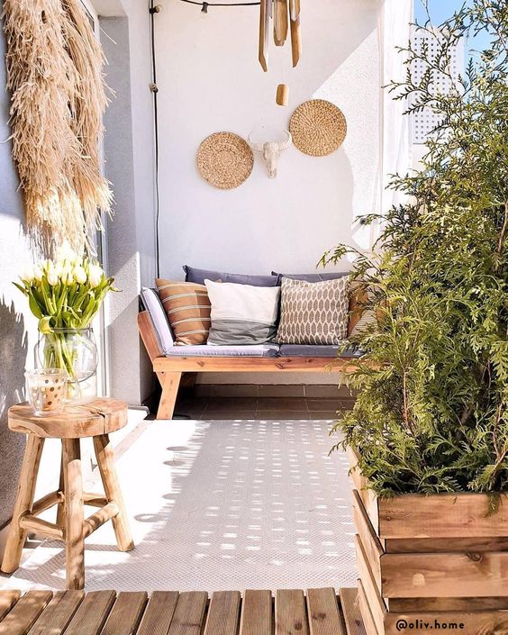 A summer balcony in neutrals, with wooden furniture, crate pots with greenery, decorative baskets, pampas grass and printed pillows.