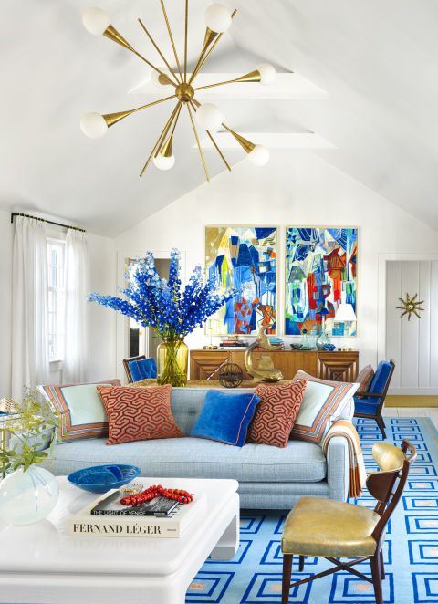 A super bold living space with bright artworks, blooms, a blue printed rug, printed pillows is a fun and bold summer space.