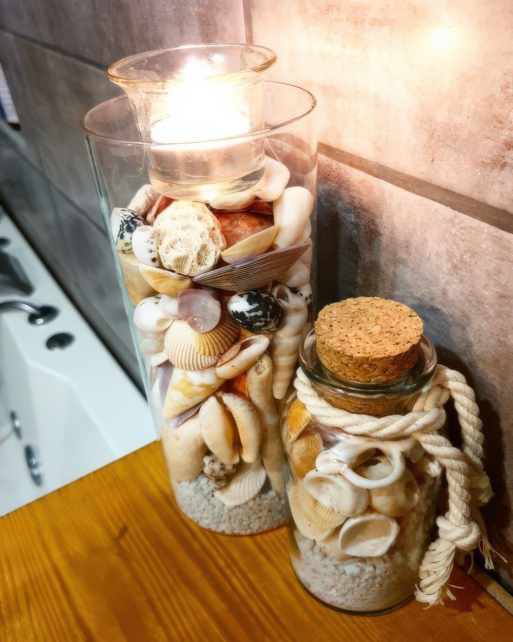 A tall vase and a bottle with beach sand and seashells plus a candle on top are a nice decoration or centerpiece.