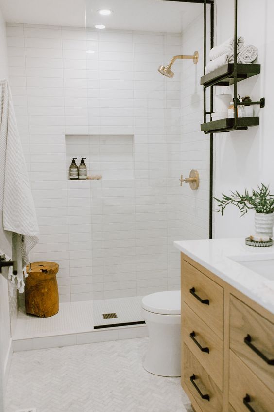 A tiny neutral bathroom clad with white long and marble tiles, a stained vanity, a wooden stool and black shelves.