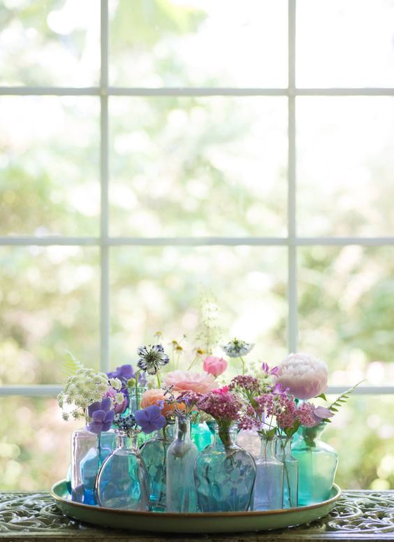 A tray with an arrangement of blue and green bottles and vases with colorful blooms.
