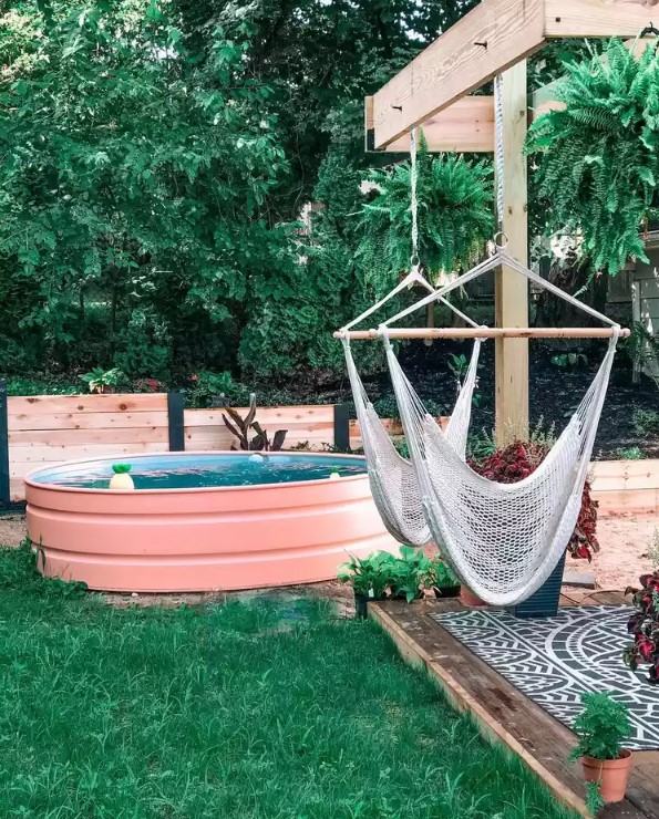 A welcoming outdoor space with a green lawn, a deck clad with tiles, with hammock chairs, a pink stock tank pool with floats.