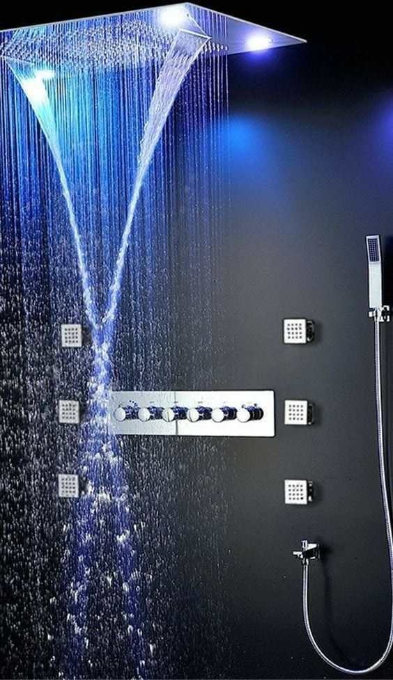A welcoming shower space wiht black walls, a large rain shower head with colored lights and stainless steel fixtures.