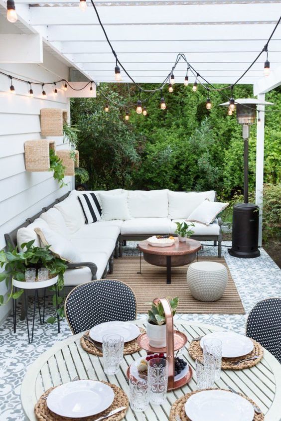 A welcoming terrace with an L-shaped bench, a jute rug, a copper table and some greenery on the wall.