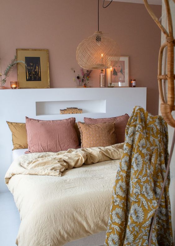 The boho headboard is done with a mauve accent wall, a bed with a white storage headboard and lovely decor, some muted color bedding.