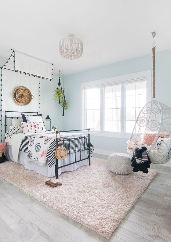 Create an airy boho teen girl bedroom with light blue walls and a canopy bed. Printed bedding, a suspended chair, and a blush rug complete the look. This design combines comfort with a touch of whimsy.