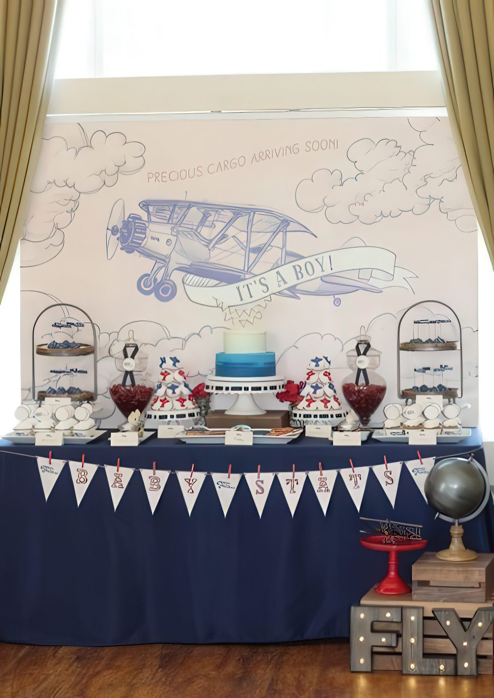 An aviation-themed dessert table with a banner, a plane backdrop, stands with sweets and cakes.