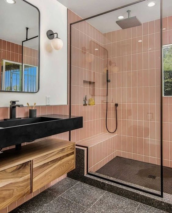 An elegant bathroom with dusty pink skinny tiles, grey terrazzo, a floating vanity, a black sink and black fixtures.