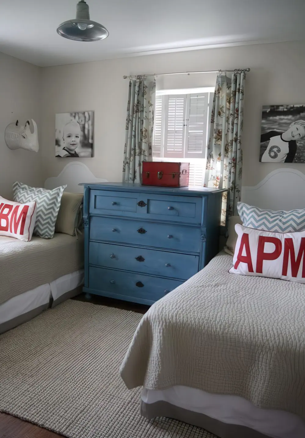 A charming shared room with twin beds flanking a bold blue dresser. The walls are decorated with black and white family photos, adding a personal touch.