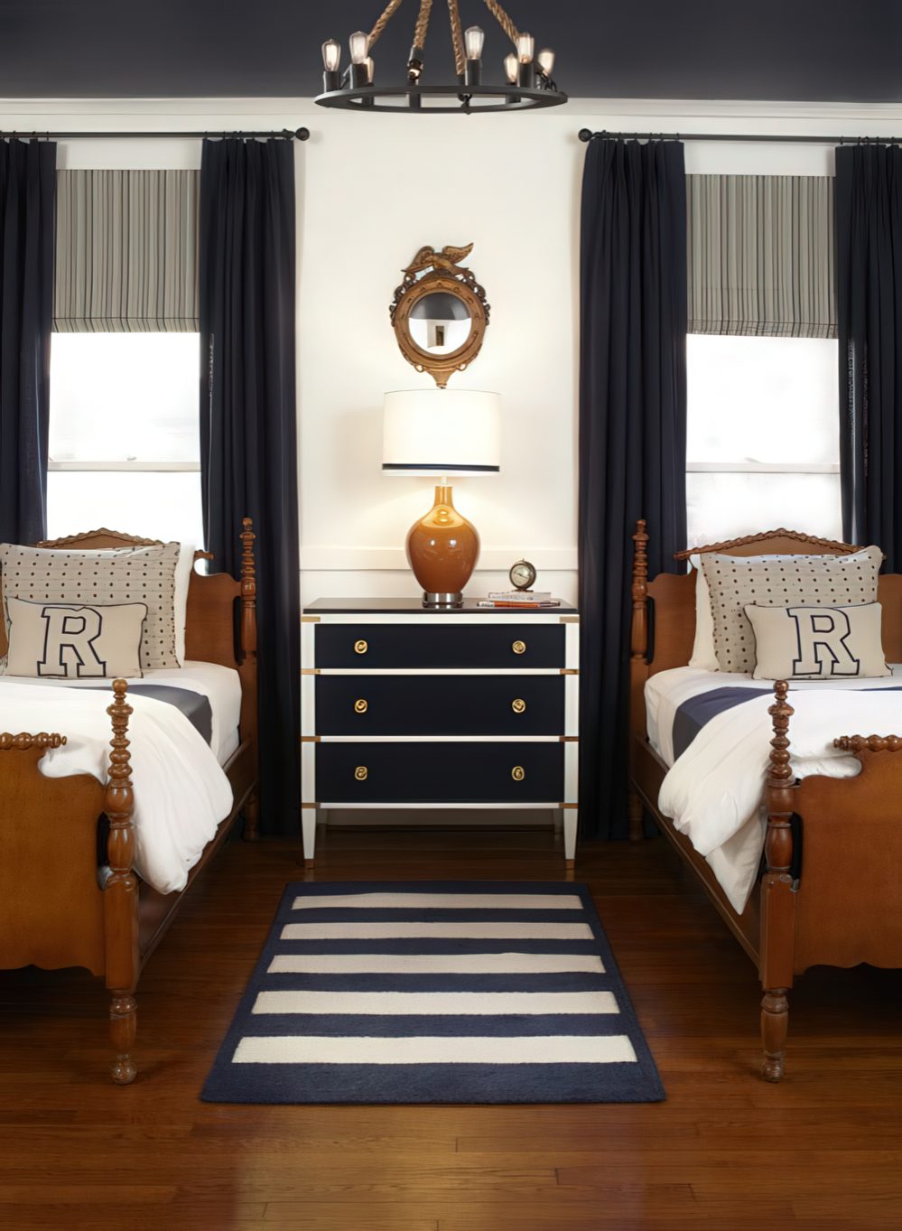 A sophisticated shared bedroom with antique wooden beds, navy curtains, and a rope chandelier. A navy and white striped rug ties the room together, giving it a refined yet cozy feel.