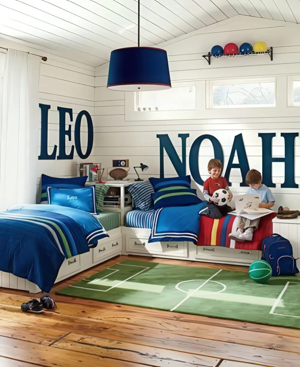 A sports-themed room with large personalized name decals on the walls, blue and green striped bedding, and a soccer field rug. The space is designed for active boys who love sports and adventure.