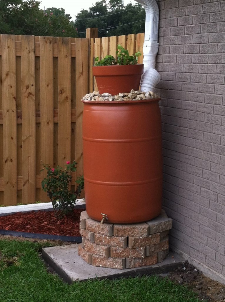 This barrel is topped with pebbles and a planter with greenery, it's raised on a brick stand.