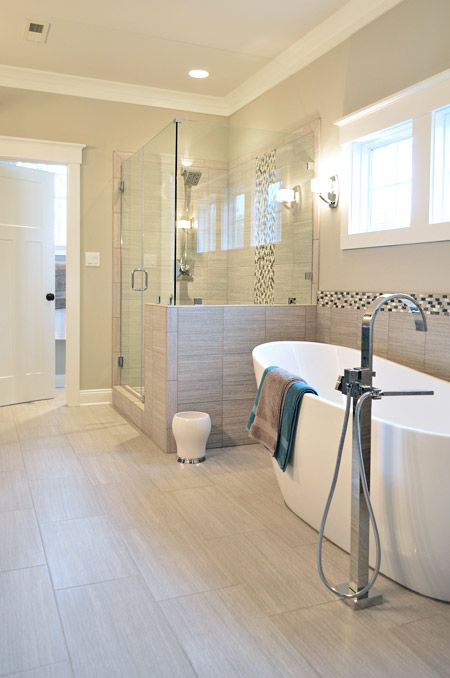 A stylish modern bathroom clad with sandy tiles, with a shower space with half walls and a lovely bathtub is filled with light.