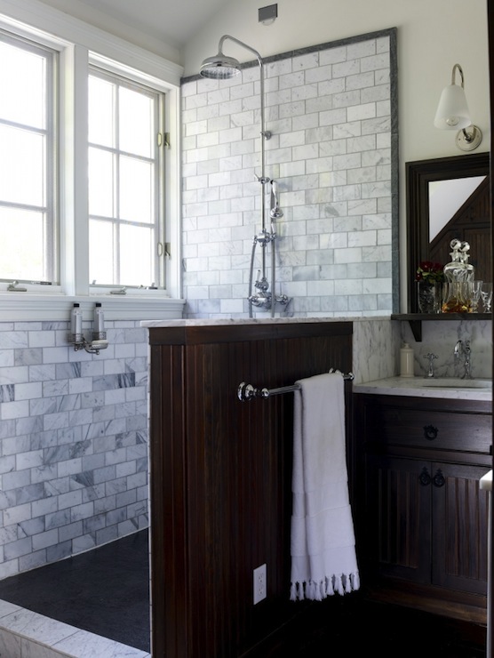 An elegant bathroom clad with marble subway tiles, with a dark half wall and a matching vintage vanity looks chic.