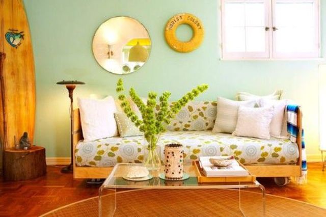 A colorful living room with mint walls, a botanical print sofa, an acrylic table, a mirror and some greenery in a vase.