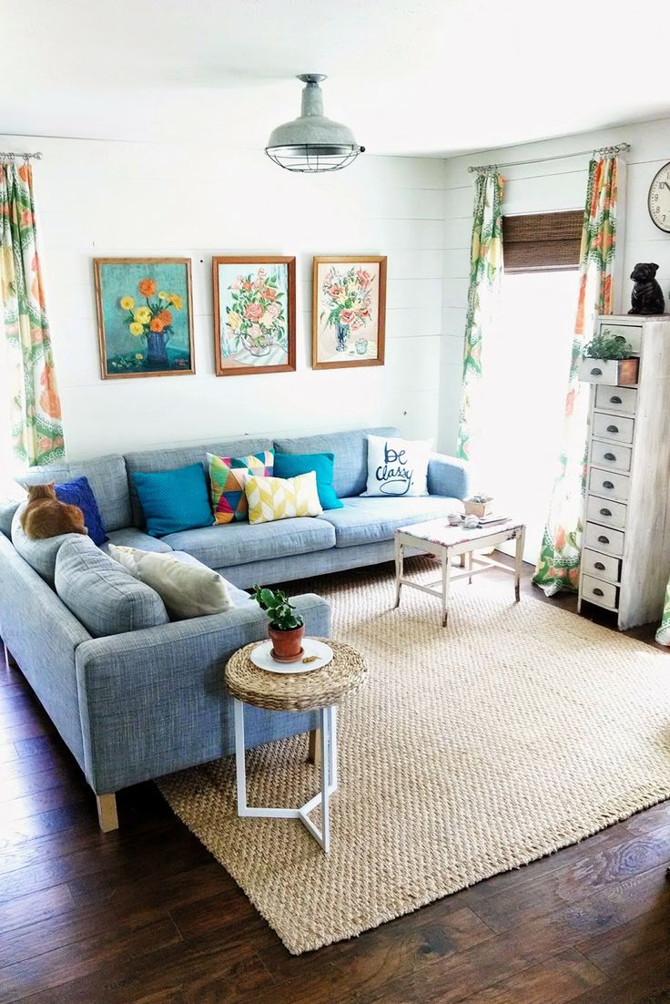 A neutral living room with a blue sofa, colorful pillows, bright printed curtains and a gallery wall for a summer feel.